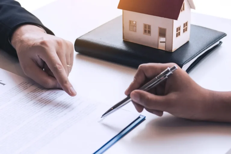 Close-up of two individuals reviewing and signing a property agreement with a miniature house model in the background
