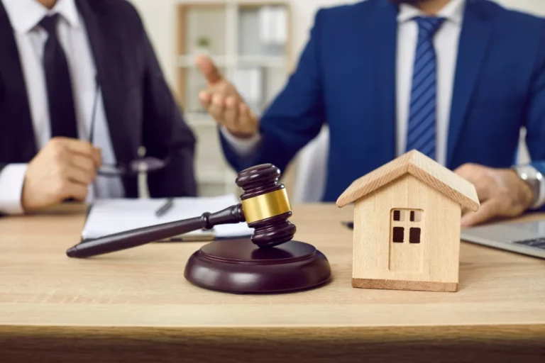 Wooden house model and gavel on a table with two business professionals discussing legal property matters
