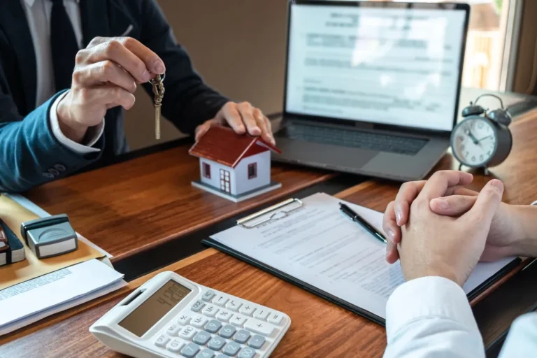 Real estate agent handing over keys beside a miniature house and legal documents during a property transaction